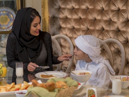 Arab woman feeding the little boy pancakes|-