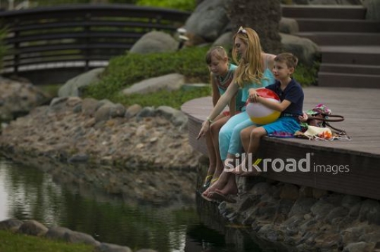 Western woman sitting by the lake with her kids|-