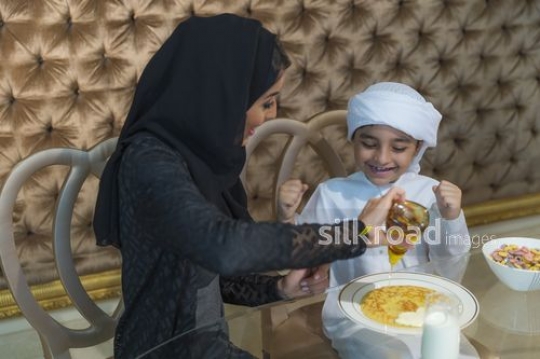 Young Middle Eastern boy sitting with his mother excited about pancakes|