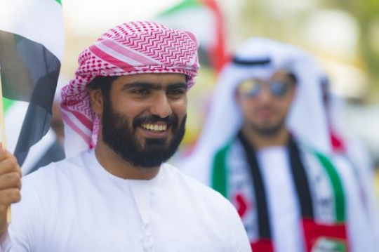Arab man walking and carrying a UAE flag at a National Day parade|