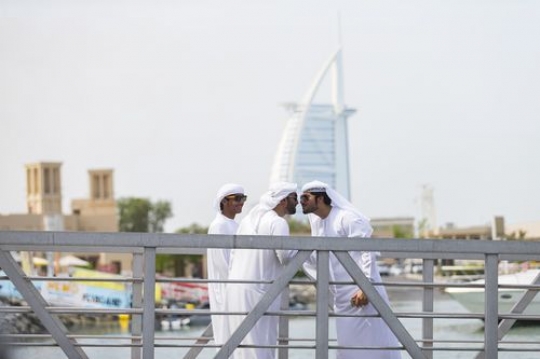 Arabian men dressed in the traditional UAE attire standing by the dock greeting each other|