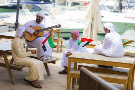 Arab men sitting on the bench together celebrating National Day|