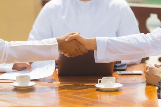 Arab business men dressed in the UAE traditional attire shaking hands after a meeting|