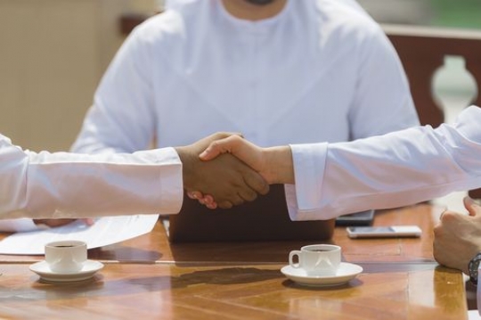 Business men dressed in the traditional UAE attire shaking hands after a meeting|