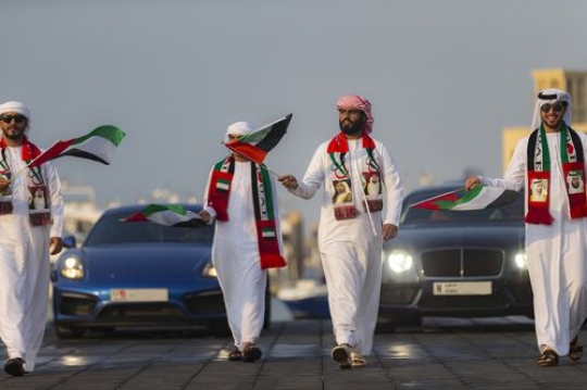 Emirati men during the National day parade followed by luxury cars|-