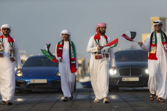Middle eastern men celebrating National day followed by luxury cars |-