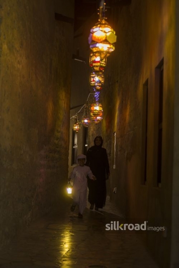 Middle Eastern son carrying a Ramadan Lantern walking infront of his mother|-
