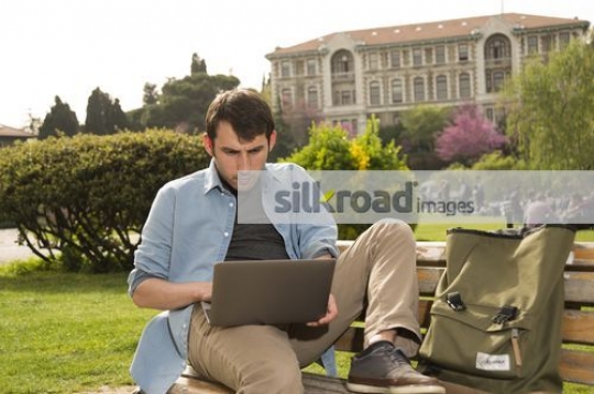Student focused on the laptop sitting on the bench|