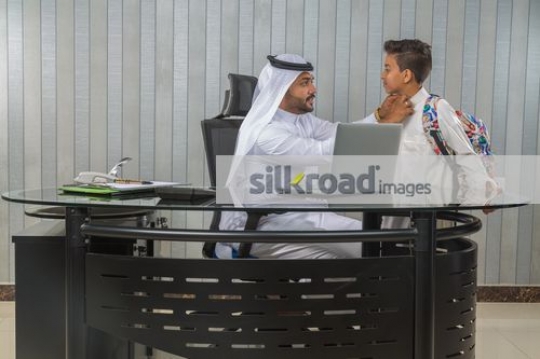 Man sitting on the chair fixing the kids kandoura