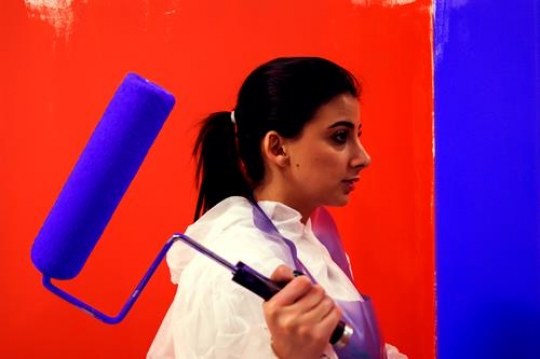woman painting a wall with red and blue paint and a paint roller