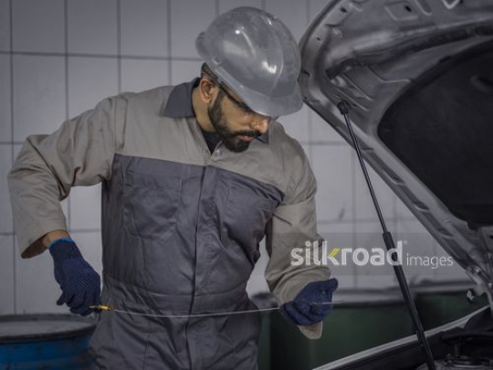 Mechanic Worker dressed in uniform checking the oil 