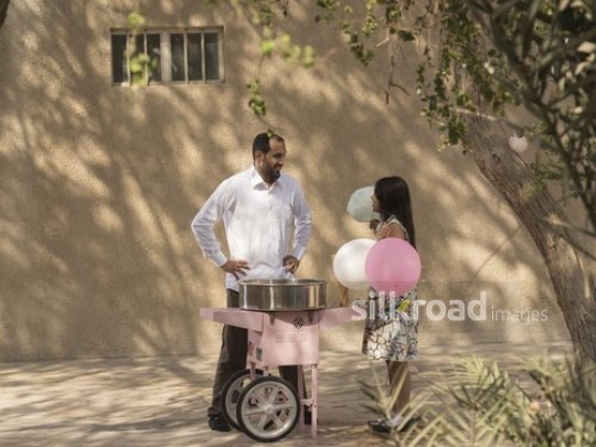 Arab man standing with the girl next to the cotton candy machine|-