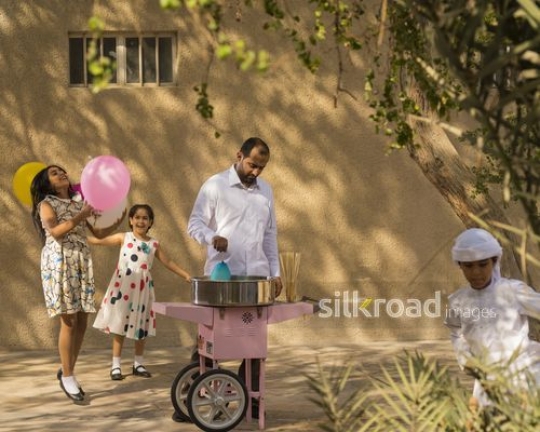 Middle Eastern man making cotton candy while the kids are playing during Eid|-