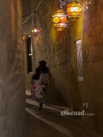 Two girls running through a pathway decorated with Ramadan lanterns