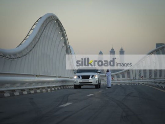 Middle Eastern man standing by the car talking on the phone|