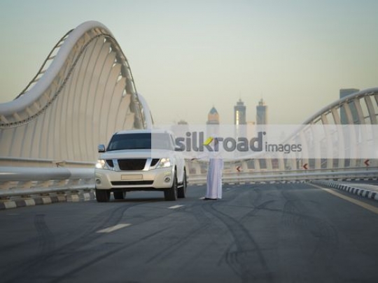 Middle Eastern man talking on the phone by the car|