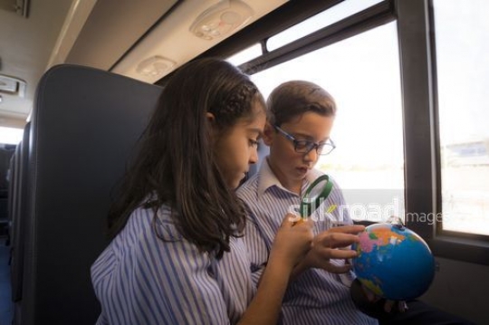 Middle Eastern Students sitting together on the bus looking at the globe|-