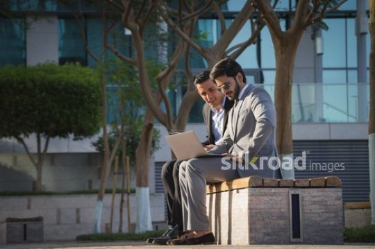 Two employees sitting down on the bench together with the laptop|-