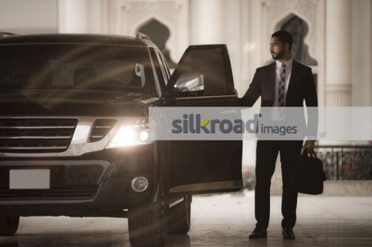 Businessman dressed in a suit closing the door of his car|