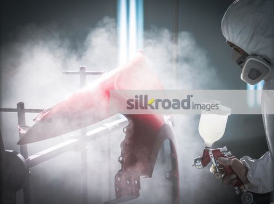 Mechanic spray painting the part of the car red|
