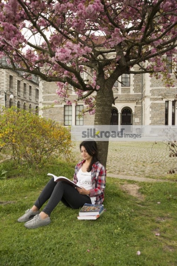 University Student leaning on the tree reading a book|