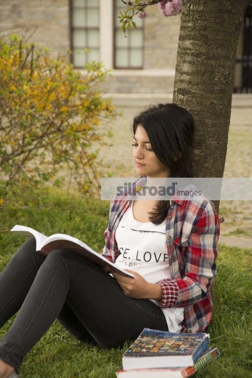 Student leaning on the tree reading her book|