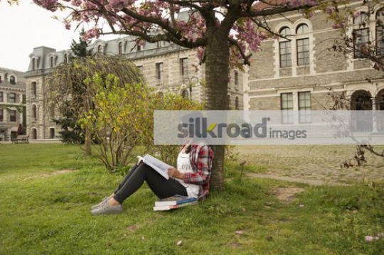University Student sitting on the grass reading her book|