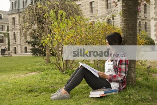 Student sitting on the grass reading the book|