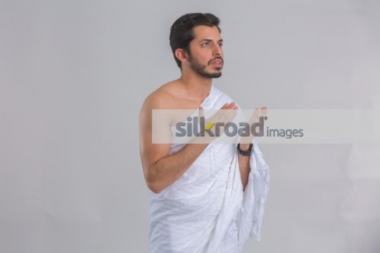 Medium shot of an Arab man dressed in the white religious attire praying|