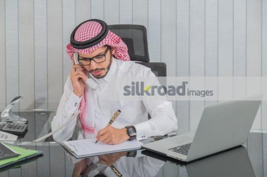 Arab Businessman talking on the phone writing notes|